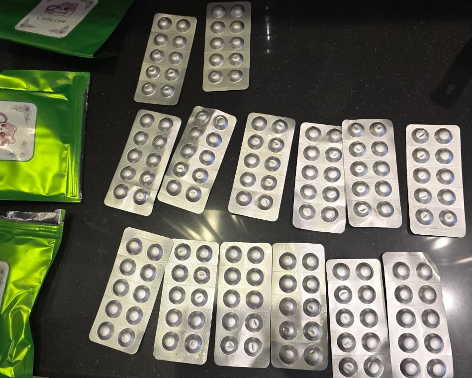 Multiple silver blister packs of round tablets arranged on a dark countertop beside green pouches.